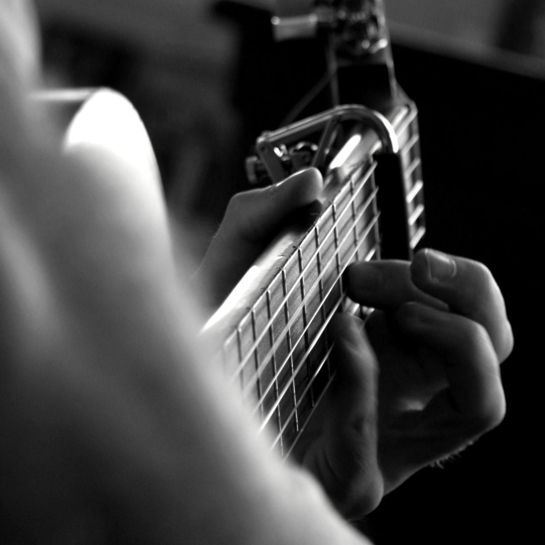 Schwarz-Weiß Bild eines Gitarrenhalses. Der Musiker greift einen Akkord mit Capodaster.