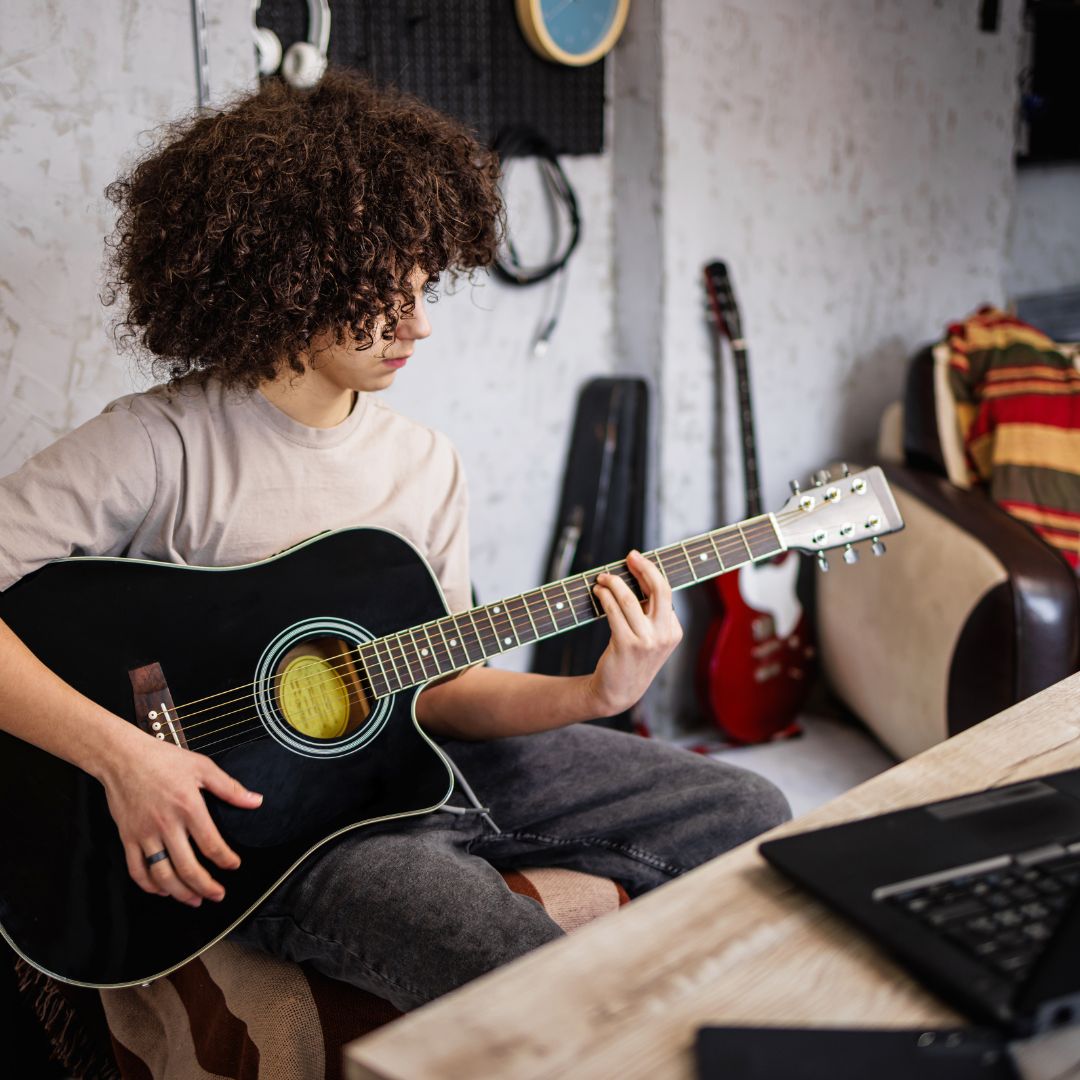Ein Jugendlicher mit dichtem Lockenkopf der Gitarre spielen übt.